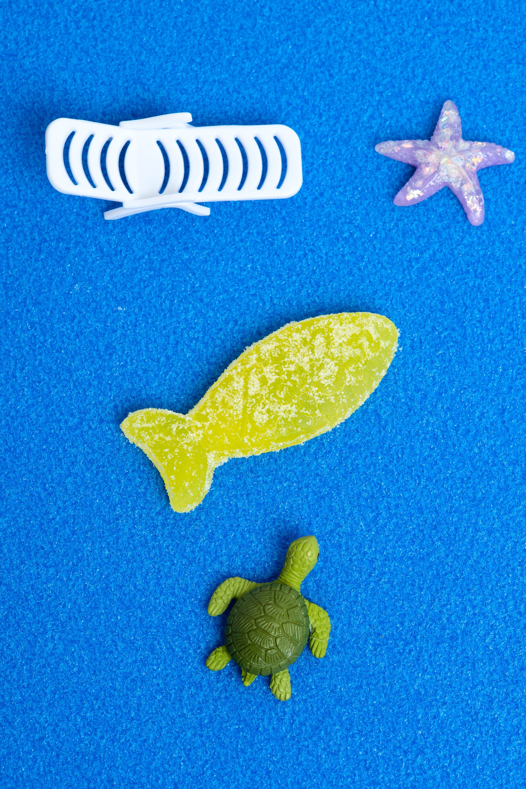 Sour Elderflower Swedish Fish by Bon Bon New York laying on a blue surface with a fake turtle and purple starfish.