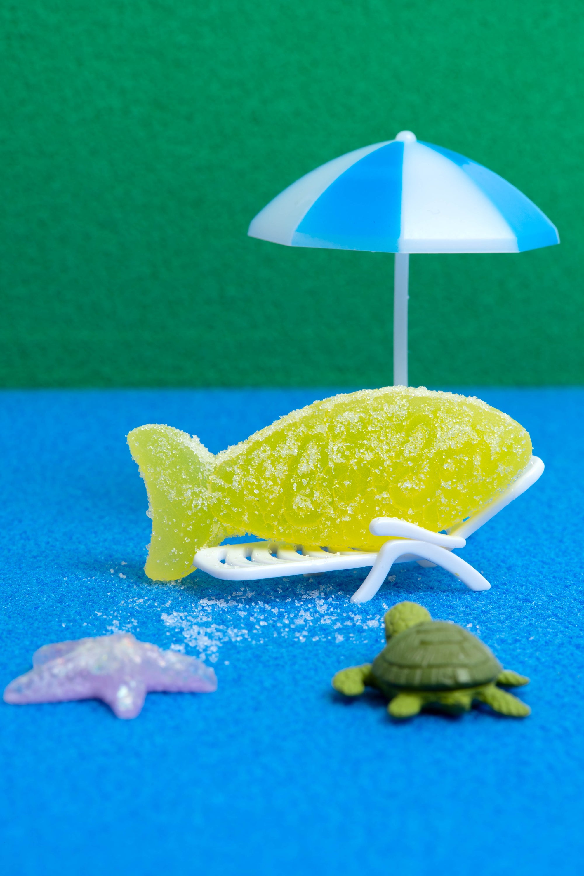 Sour Elderflower Swedish Fish by Bon Bon New York lounging on a chair with a staged beach background.