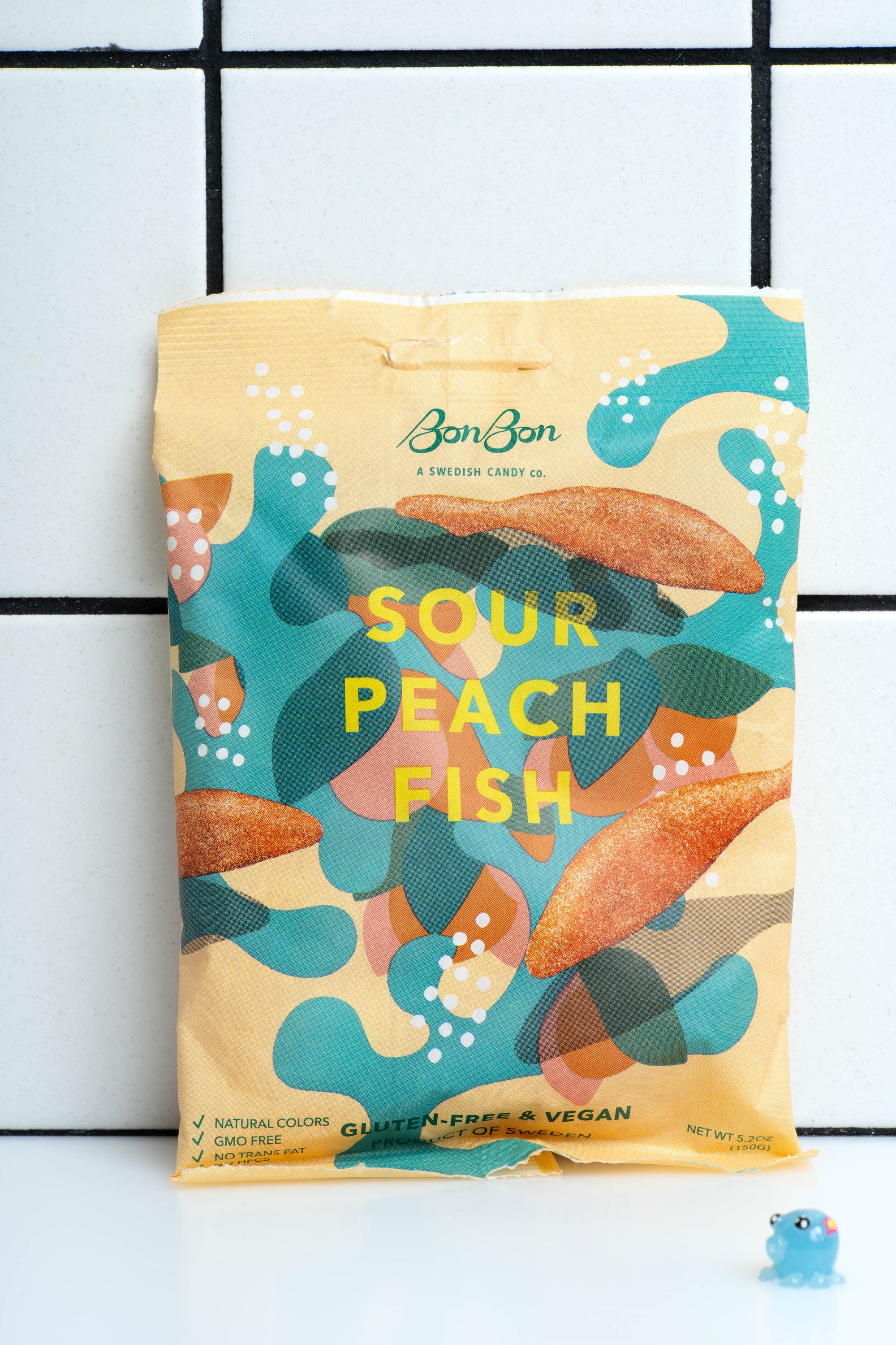 
    
        Sour Peach Swedish Fish by Bon Bon New York packaged in a light yellow bag with teal designs and text text.
    
  